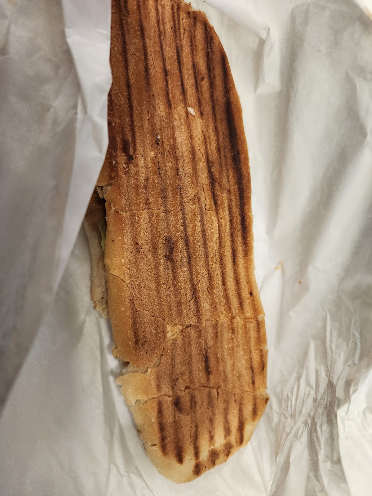 A pressed Abou Afif sandwich, grill marks across the bread, on wrap paper