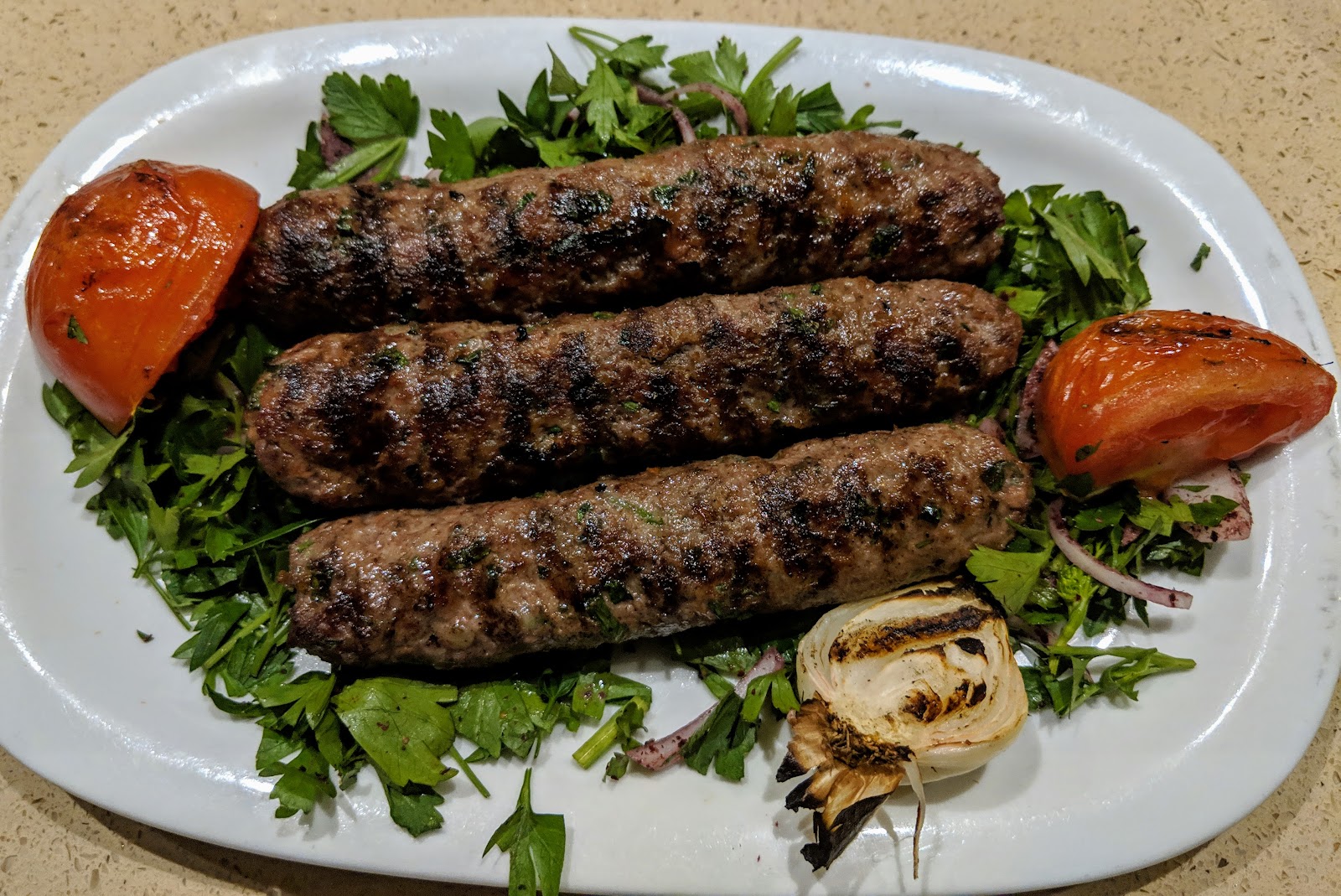 Three kofta skewers with grilled tomato on parsley