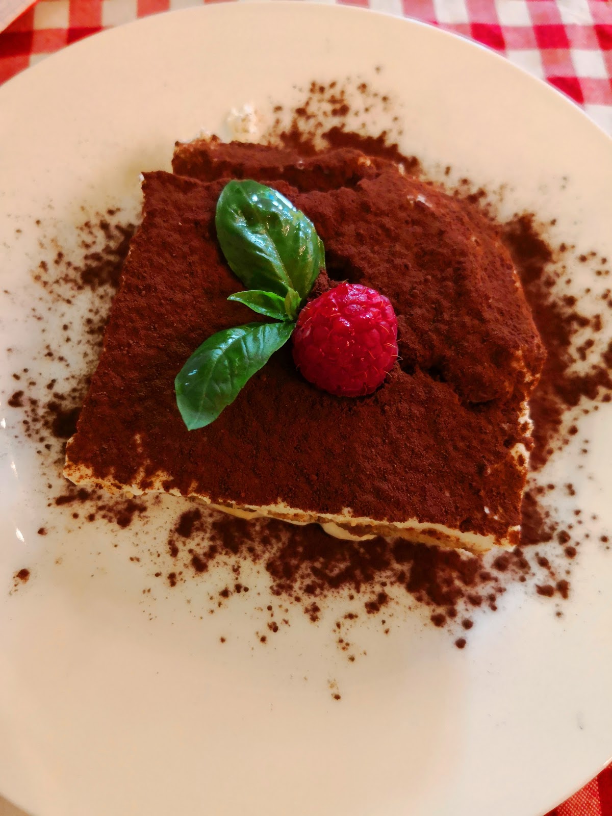 A square of tiramisu with cocoa and one raspberry