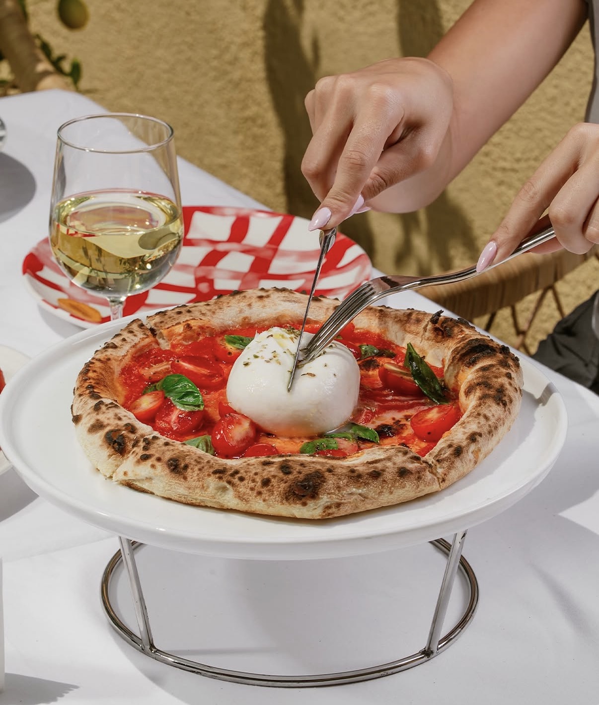 A pizza served with a whole burrata being cut at the table