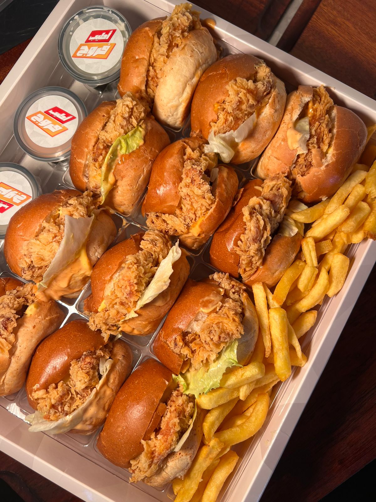 A takeaway box of crispy chicken sliders, fries and garlic pots from above