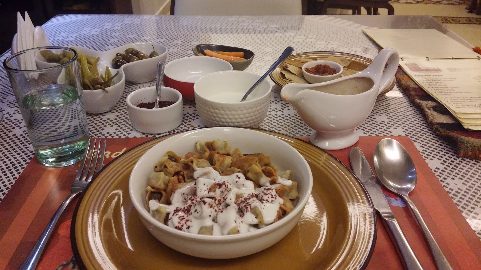A bowl of mante under yogurt and sumac, served with pickles