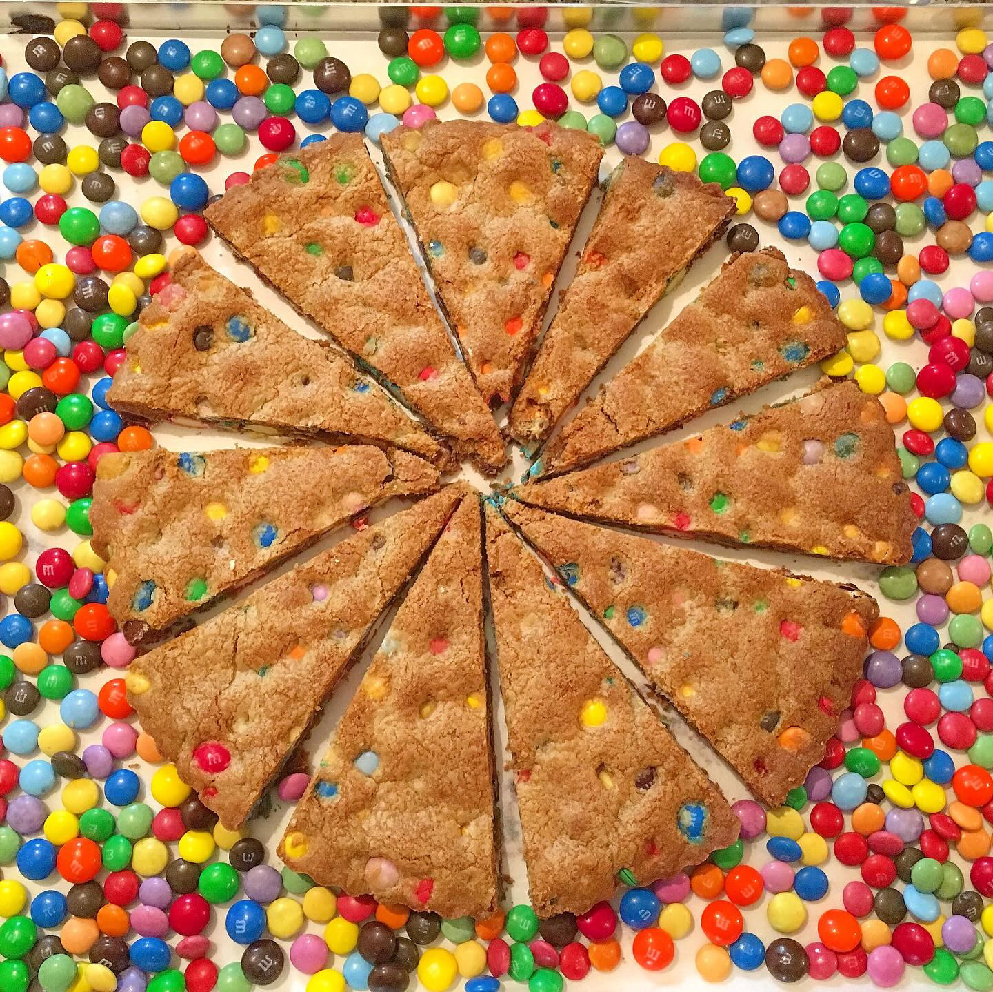 A giant cookie pizza cut into wedges inside a ring of candy