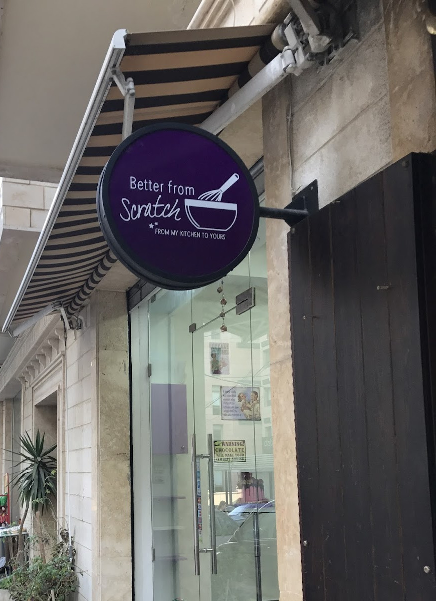 The round Better From Scratch sign hanging over the sidewalk in Mina El Hosn