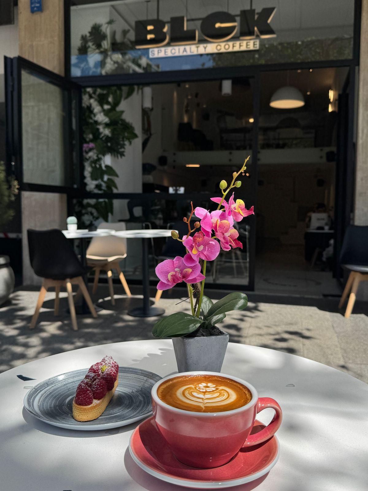 A flat white and a glazed tart on the outdoor table by the entrance