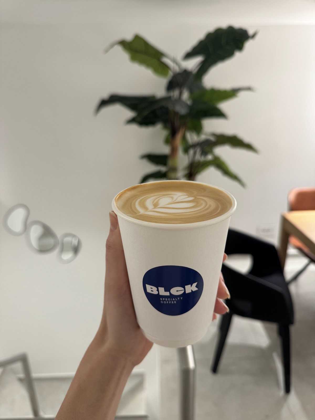 A hand holding a BLCK paper cup with latte art