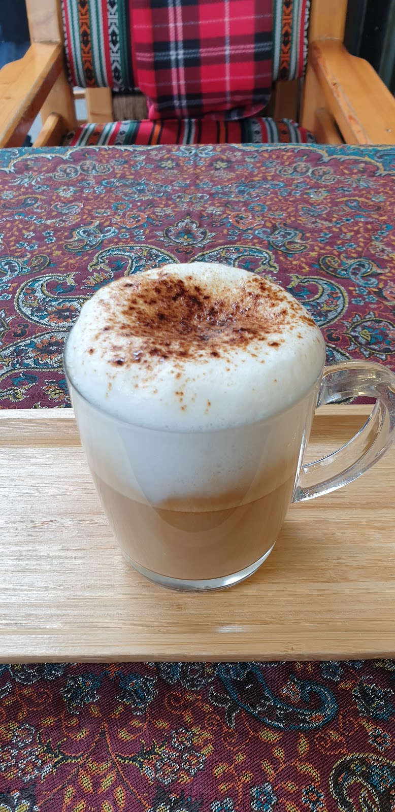 A cappuccino on a wooden board beside the tartan chair