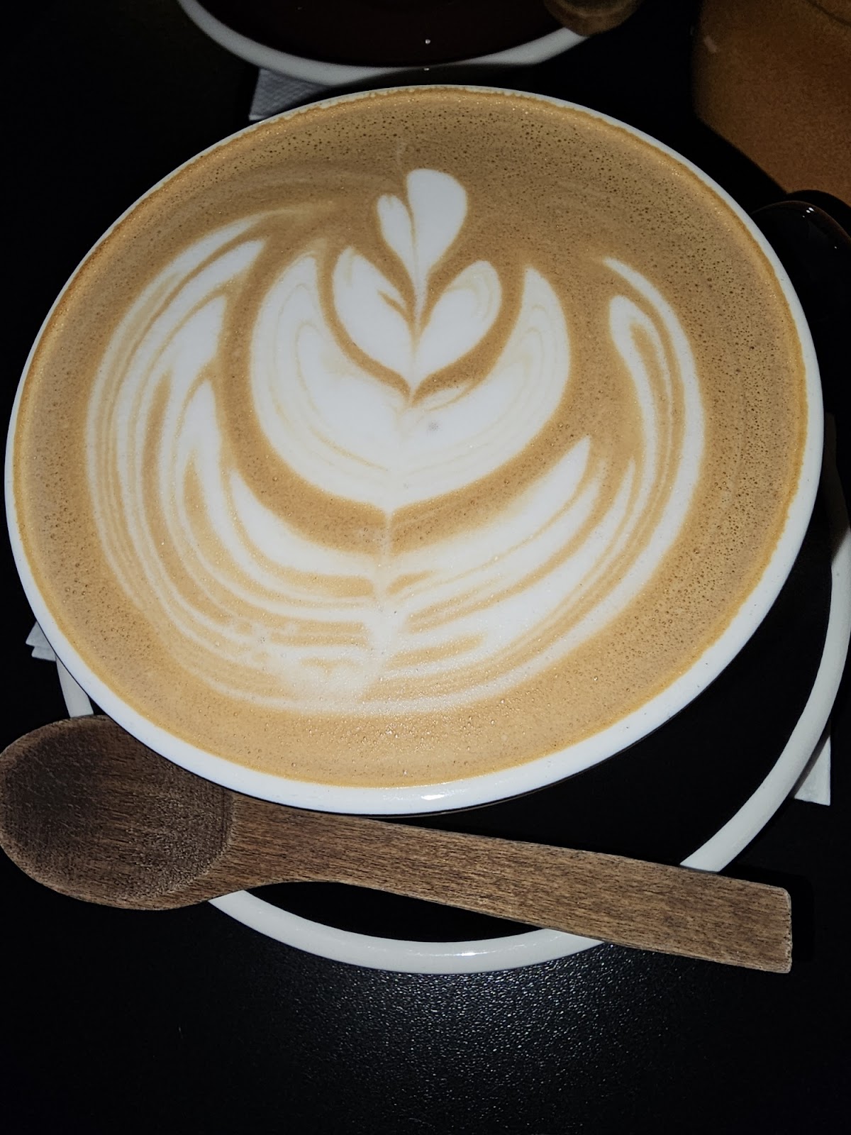 Latte art rosetta in a wide cup with a wooden spoon