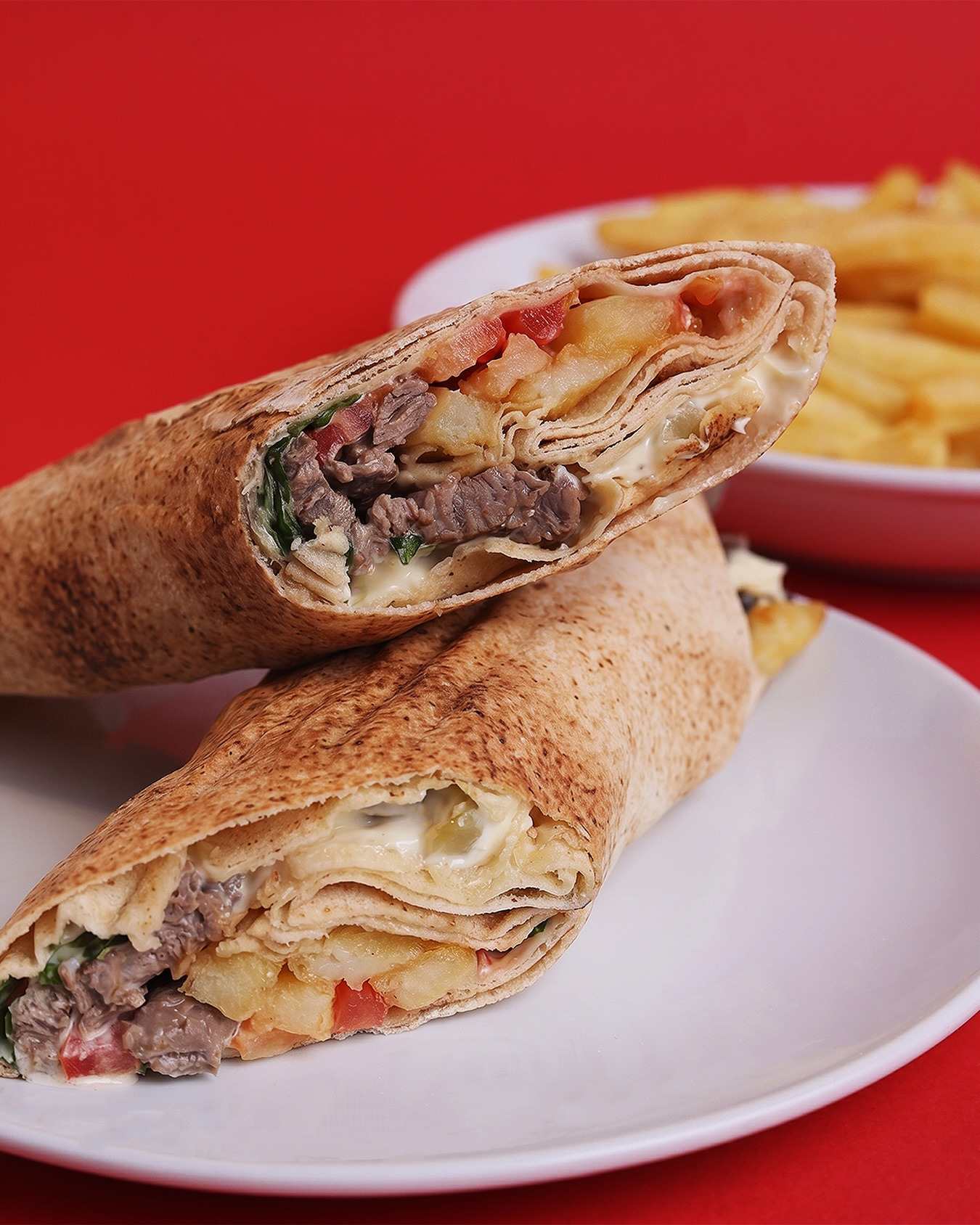 Two halves of the Chaud Froid fajita sandwich stacked on a white plate against a flat red field