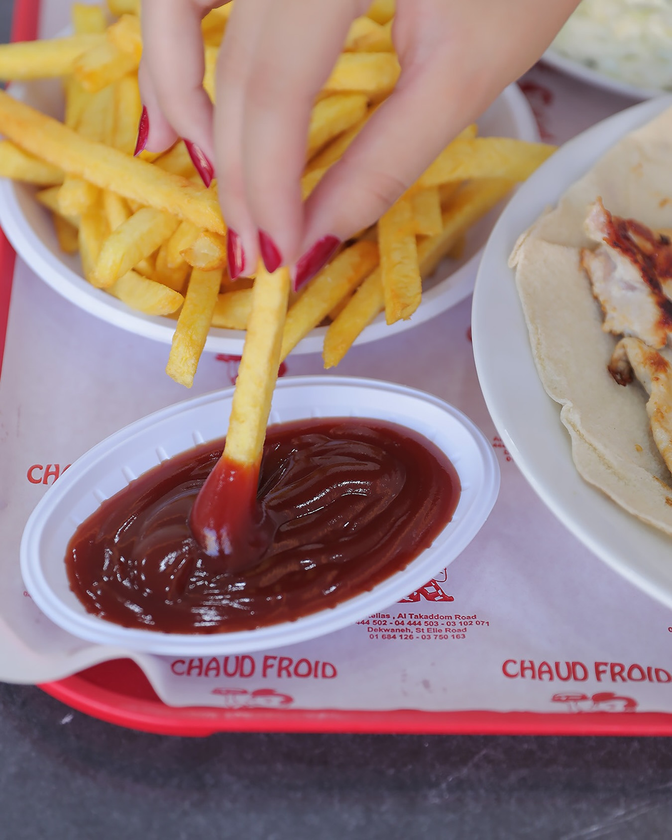 A hand dipping a chip into ketchup on the printed Chaud Froid tray
