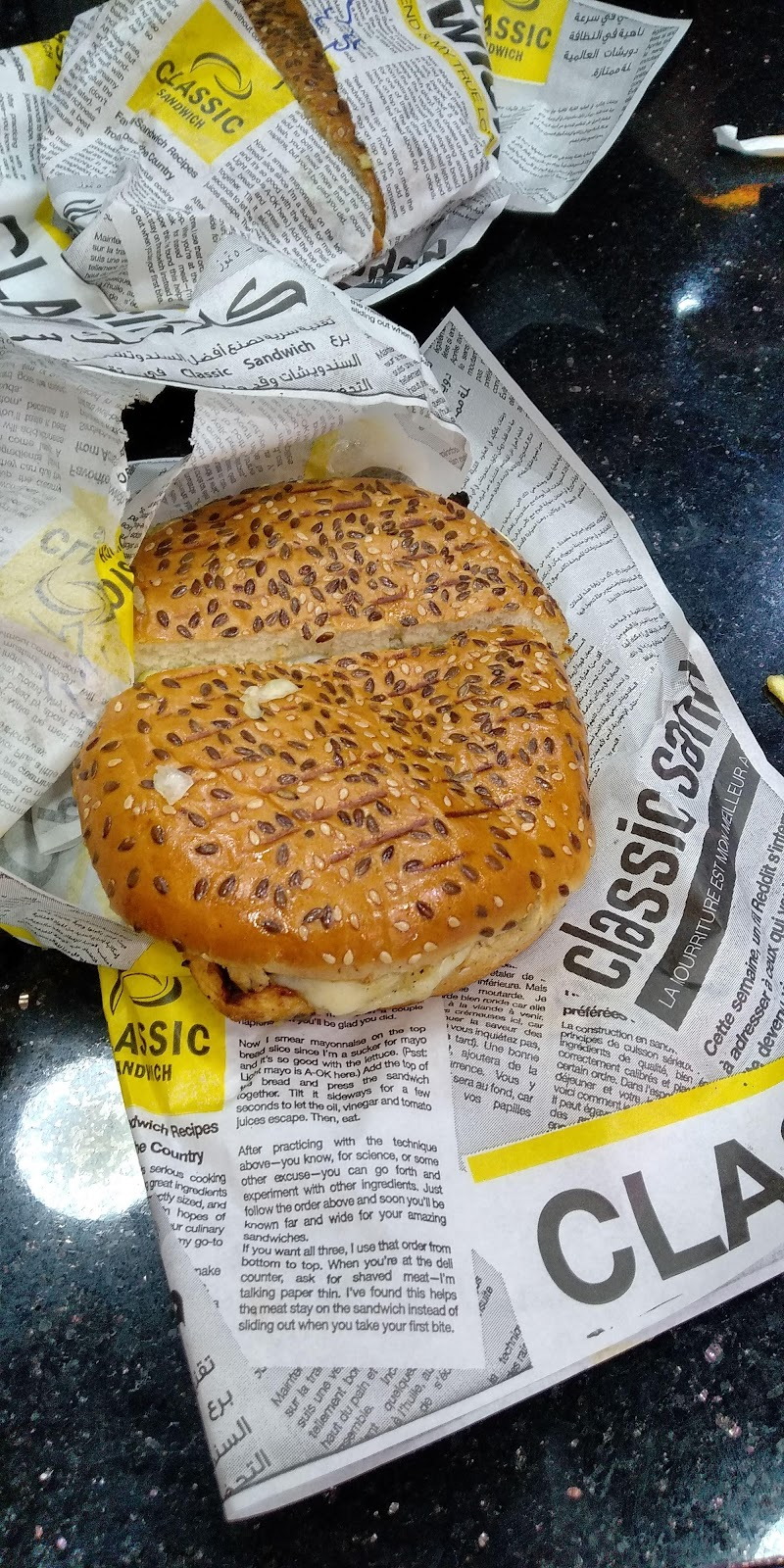 A sesame bun sandwich sitting open on the shop's own printed wrap
