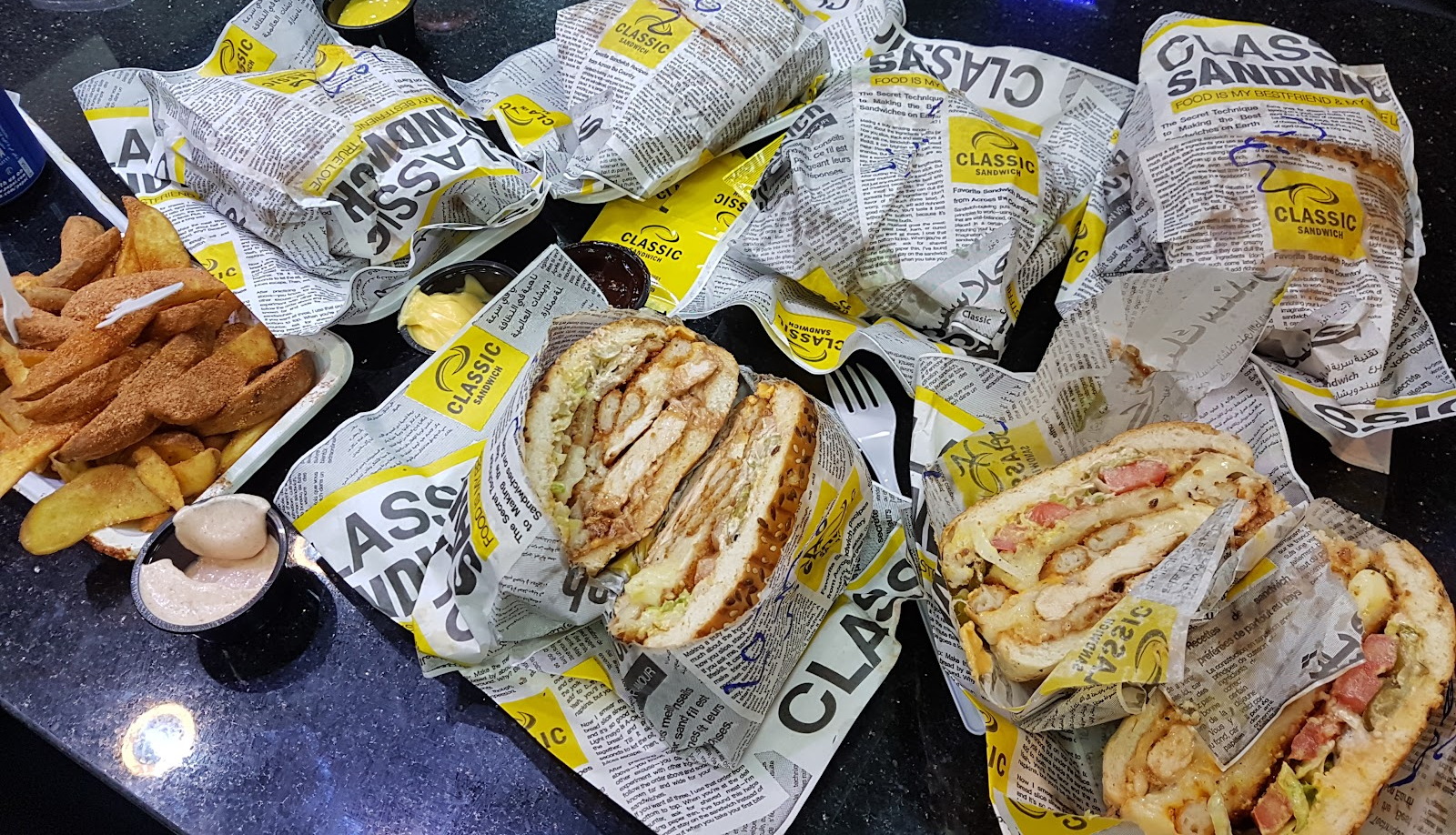 A table covered in orders still folded in the printed wrap, with a plate of fries