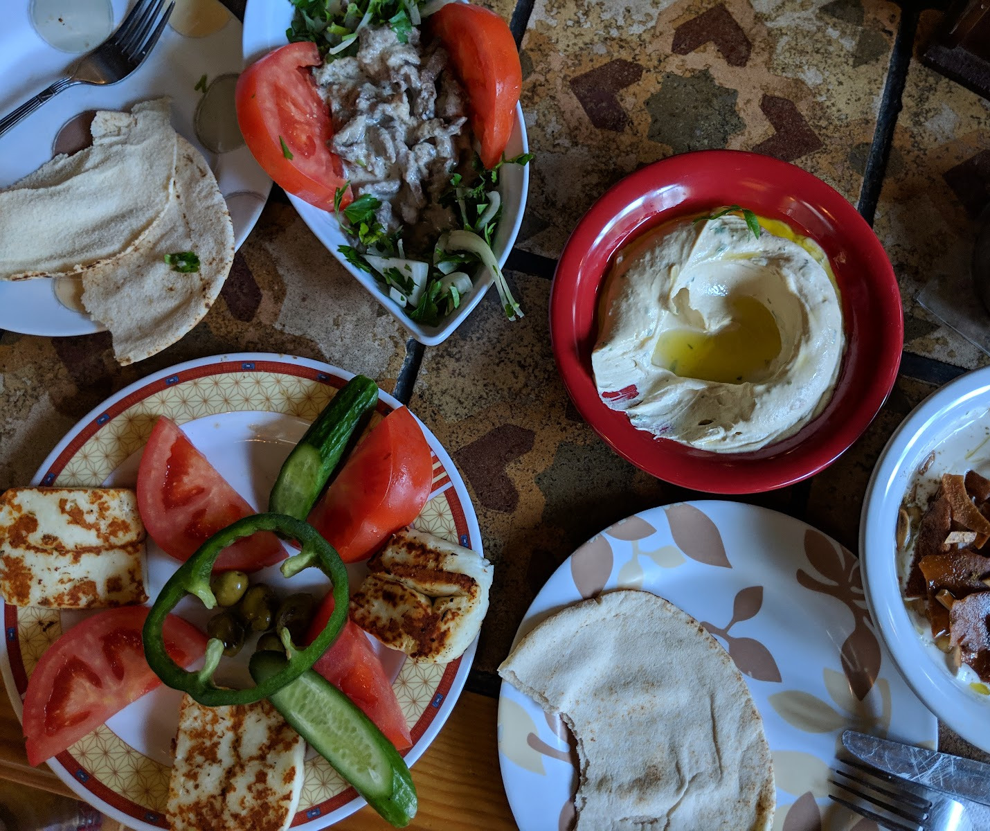 An Em Nazih mezze spread photographed from above: hummus in a red bowl, tomatoes, peppers and bread across the table