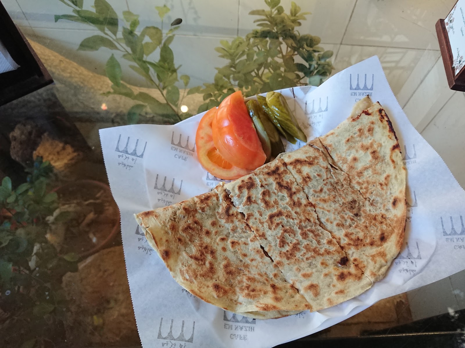 A folded saj wrap on paper with tomato and pickles
