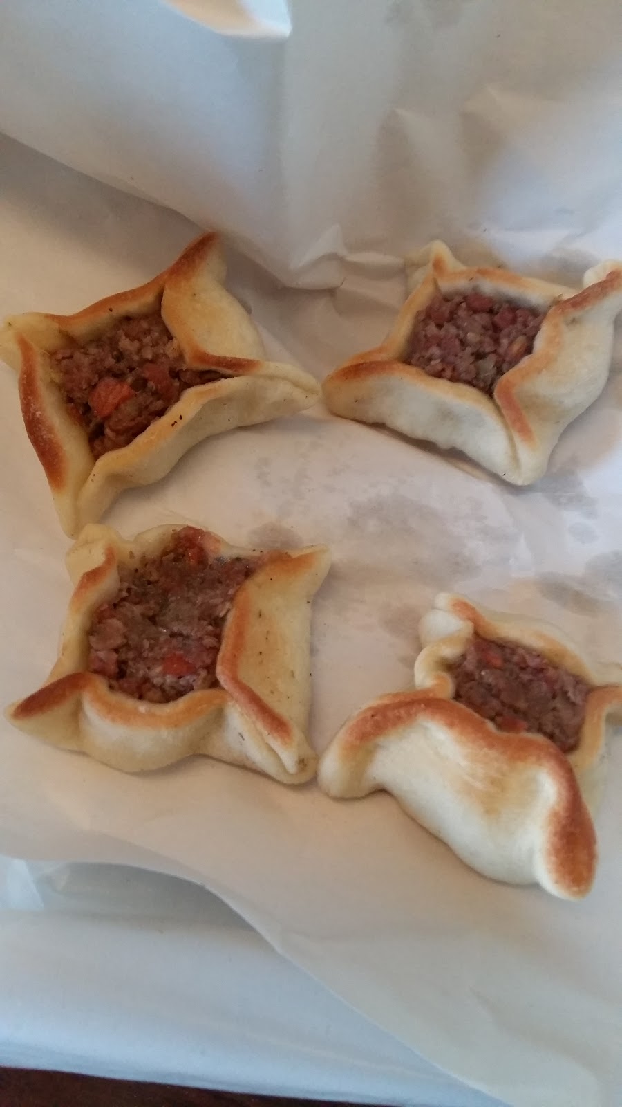 Four square-pinched meat sfiha on white paper