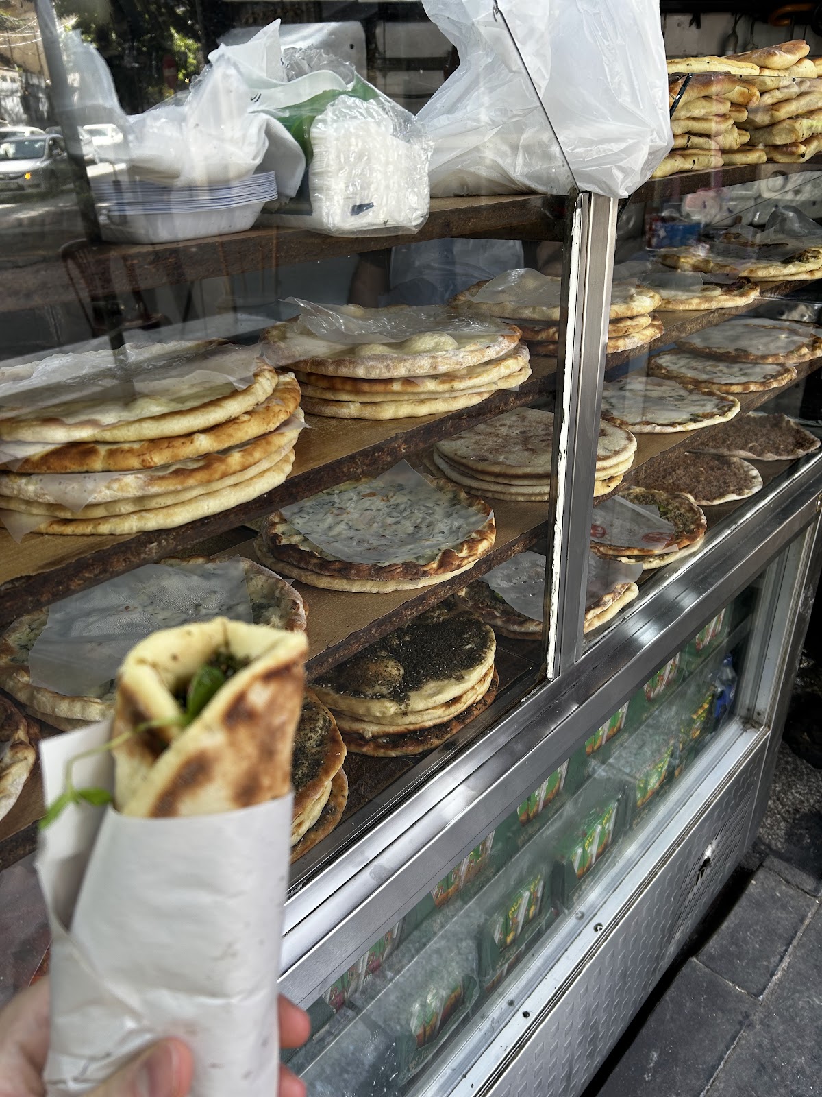 Stacked manakish trays behind the counter glass, one wrapped to go