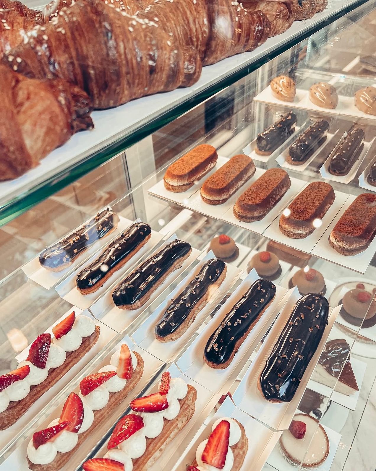 Rows of eclairs and strawberry tarts inside the display, seen through the glass