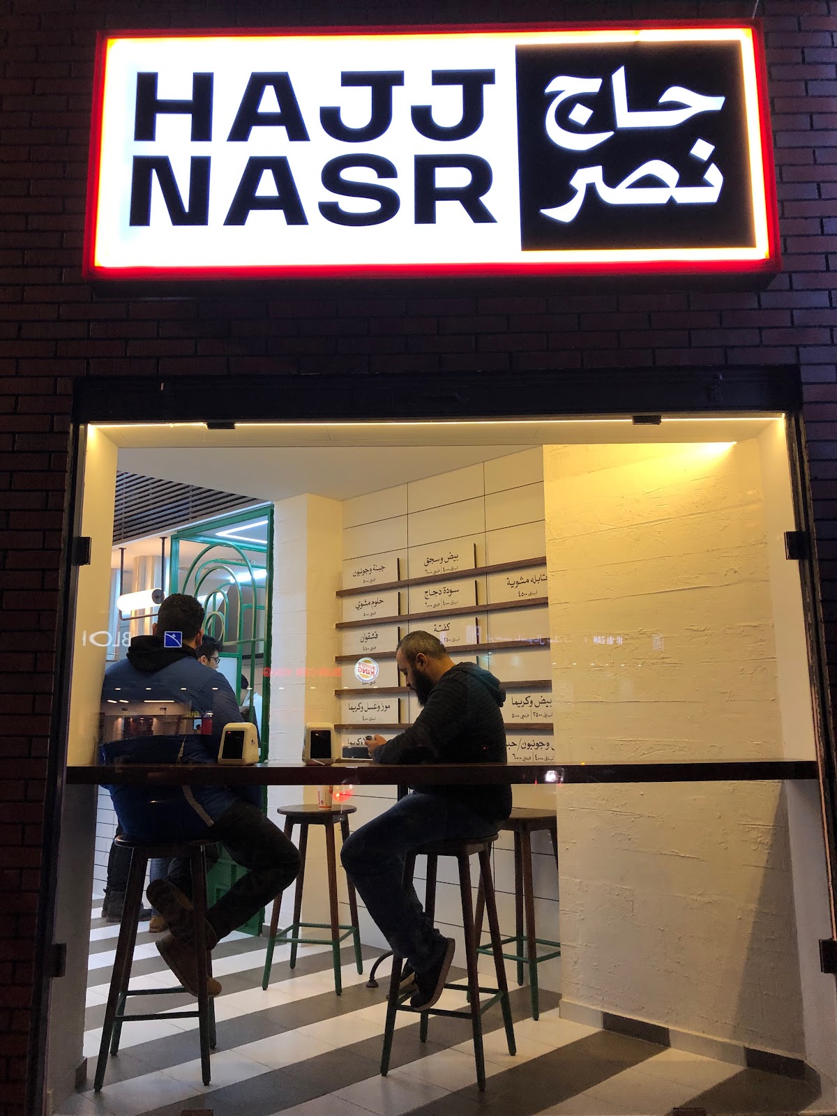 The lit Hajj Nasr sign over the shopfront on Sassine Square at night