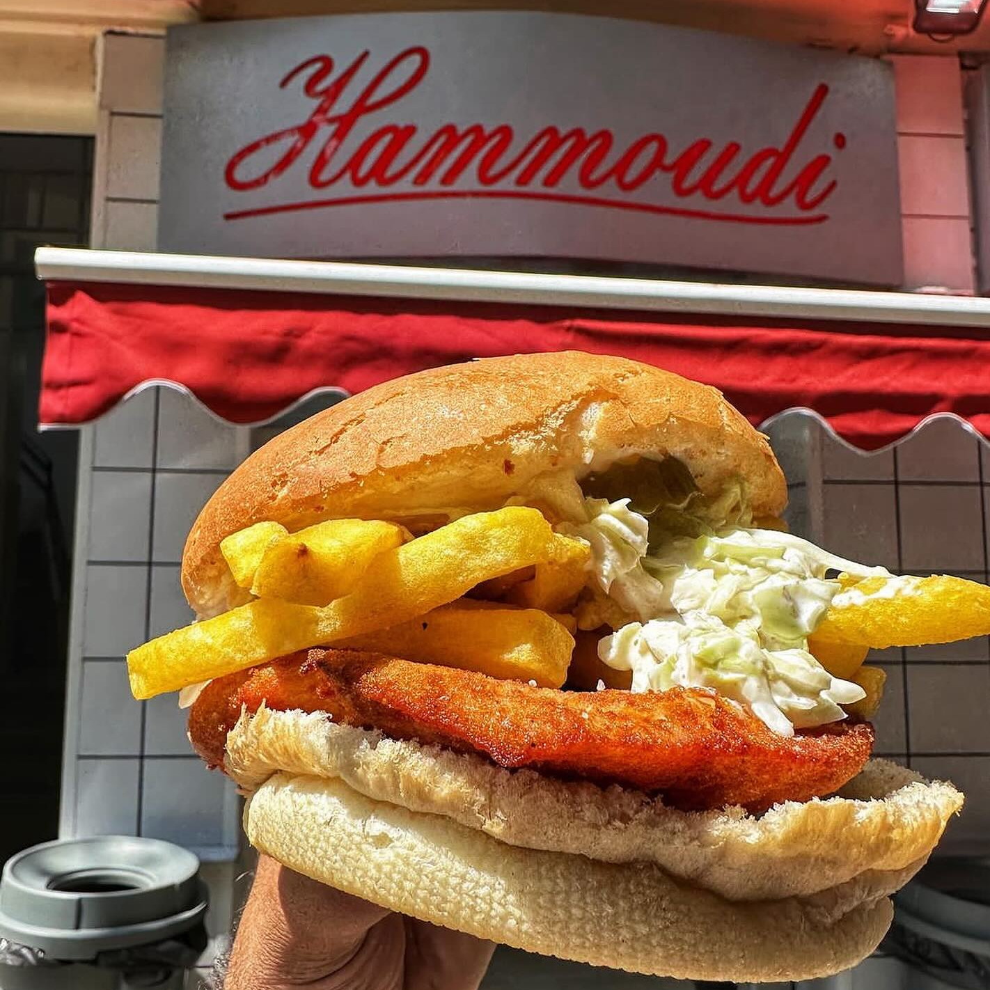 The escalope sandwich held up under the Hammoudi sign, fries and coleslaw inside the bread