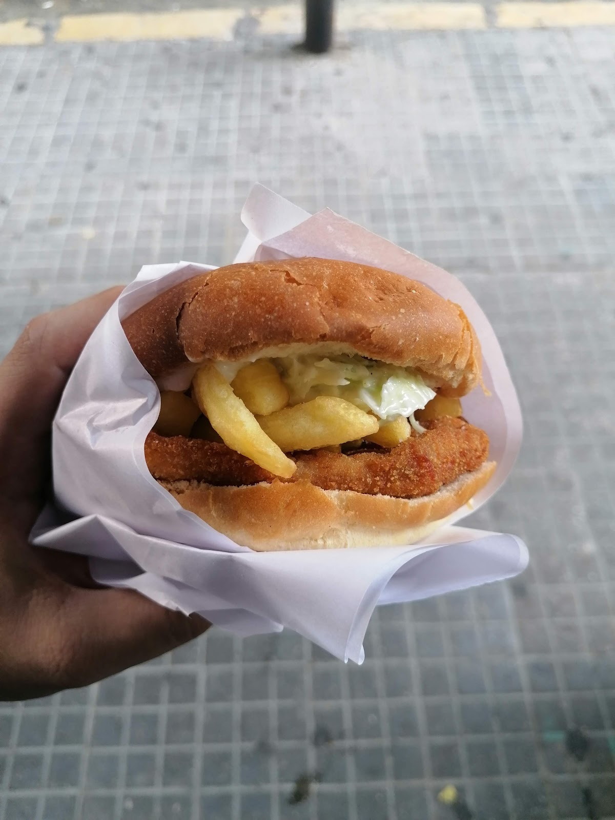 A hand holding the escalope sandwich wrapped in paper on the pavement