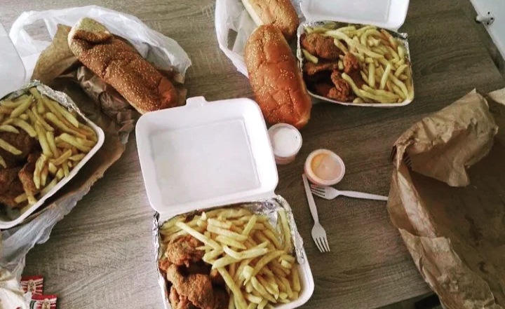 A meal set out to eat in: sandwiches, a burger, fries and chicken tenders in their boxes, sauces and a fork