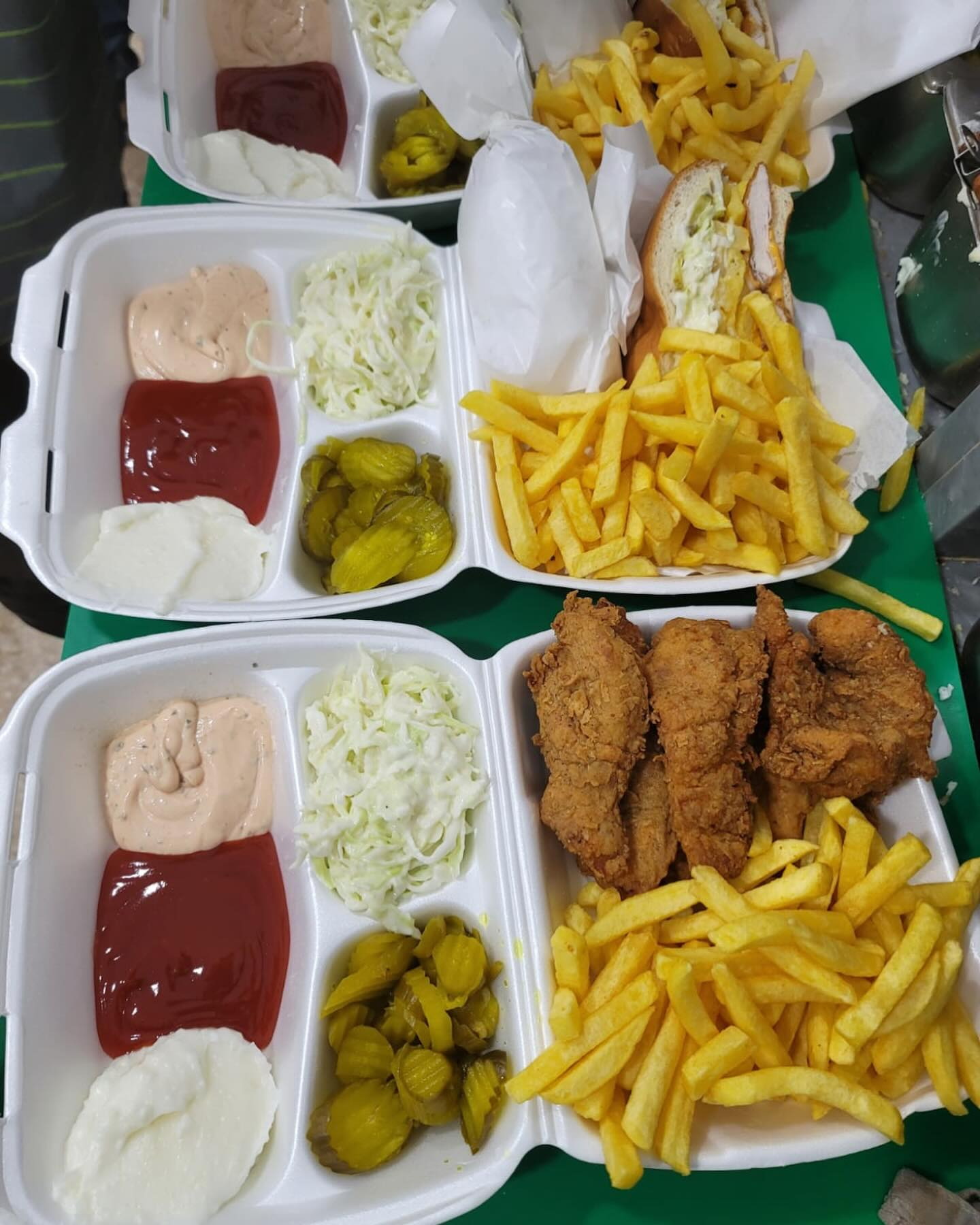Takeaway boxes with chicken tenders, fries, coleslaw, pickles and sauces