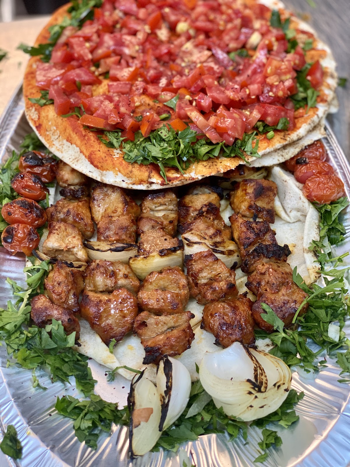A kebab platter on flatbread with grilled tomato and parsley
