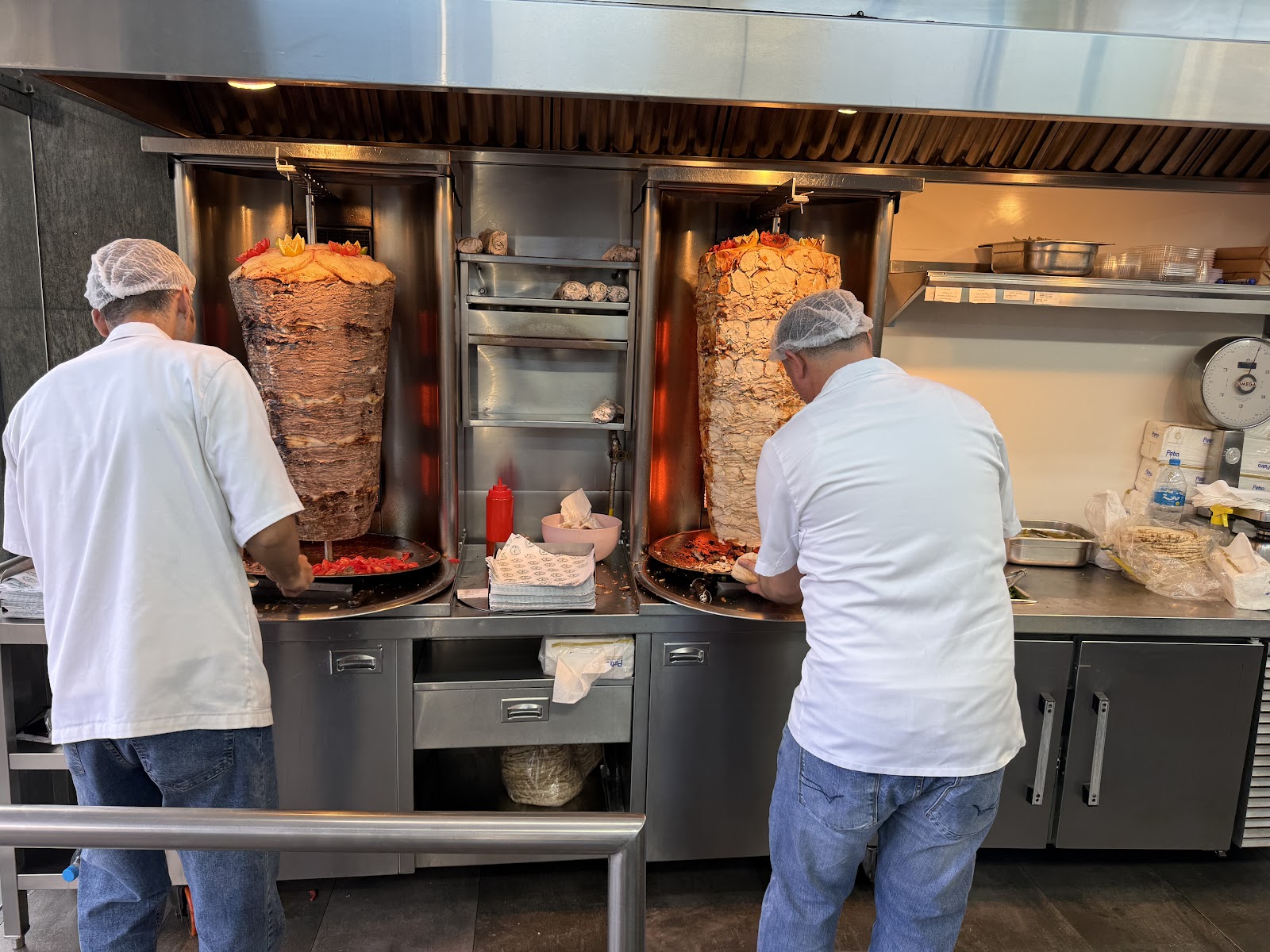 Two masters at the twin shawarma spits, backs to the room