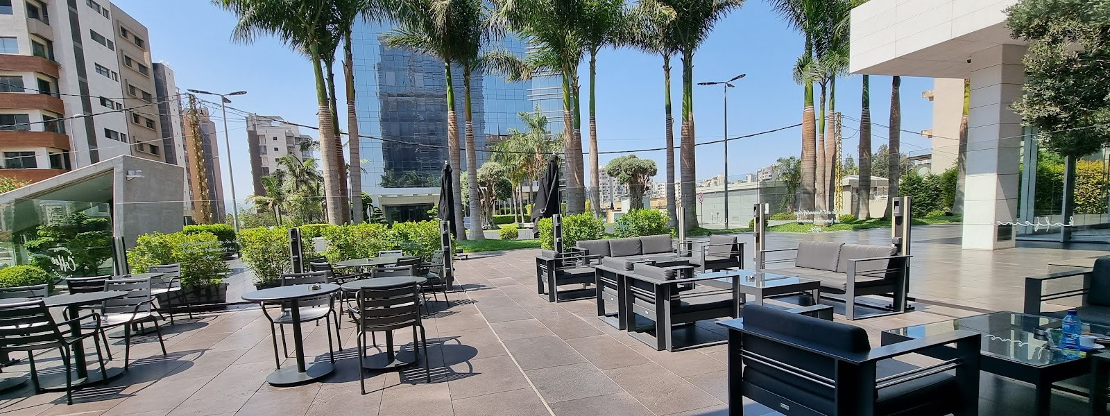 The Kaffeine terrace, black tables under palms with the office towers of Horsh Tabet behind