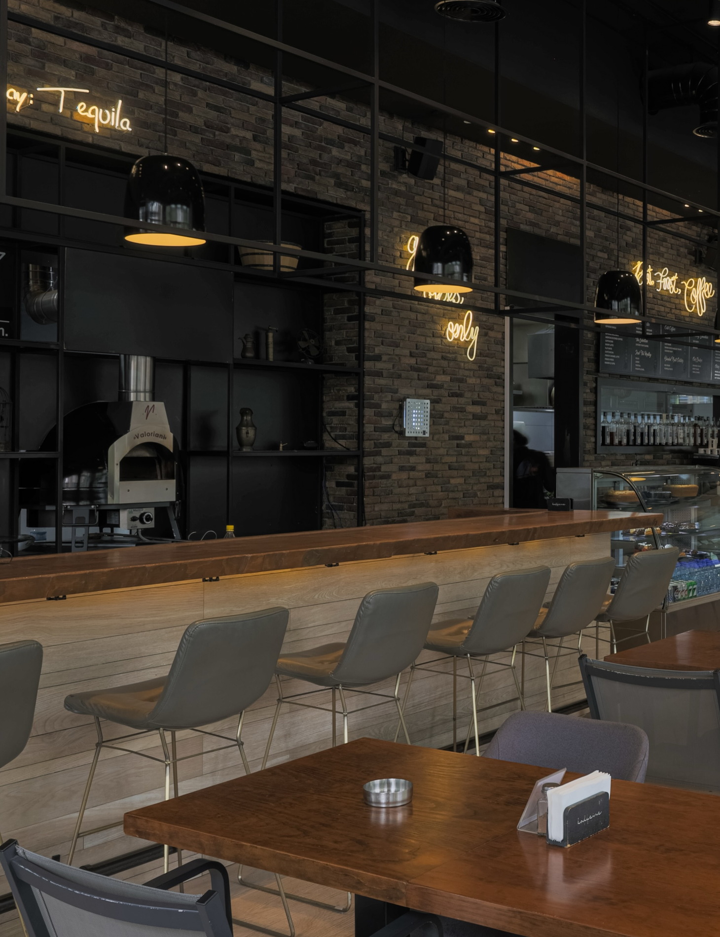 The long wooden counter, grey stools and the neon script on the black brick wall inside Kaffeine