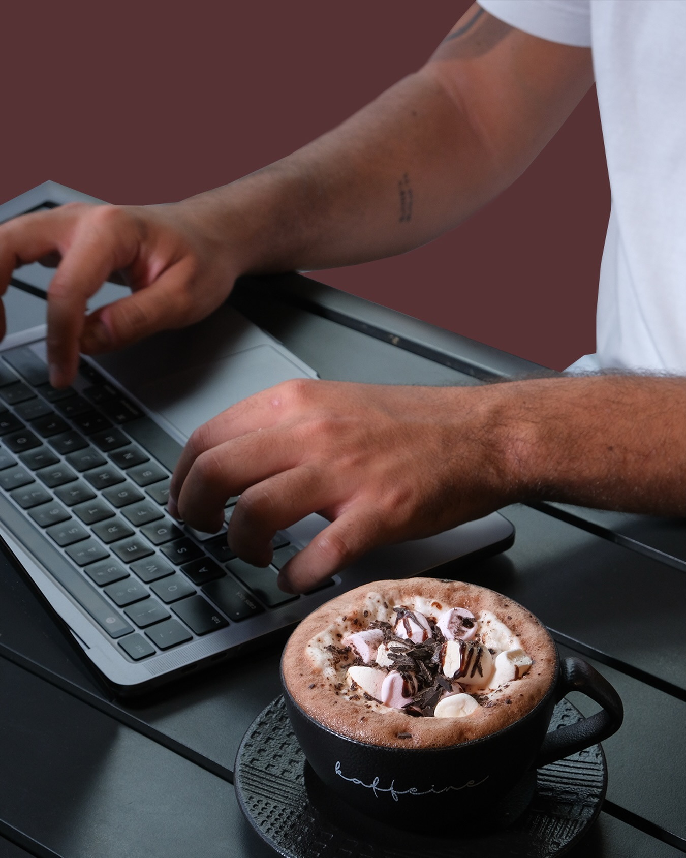 Hands typing on a laptop beside a Kaffeine mug of hot chocolate