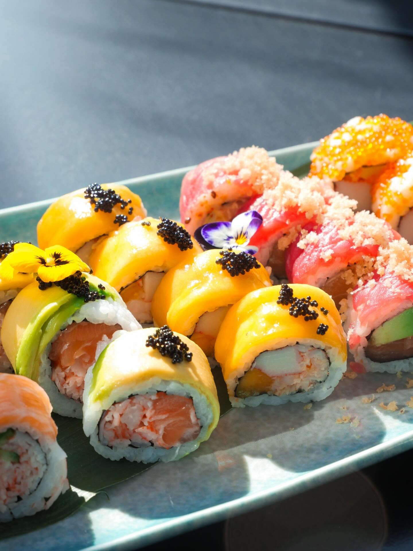 Signature KAMI rolls topped with mango, avocado and caviar on a long teal plate