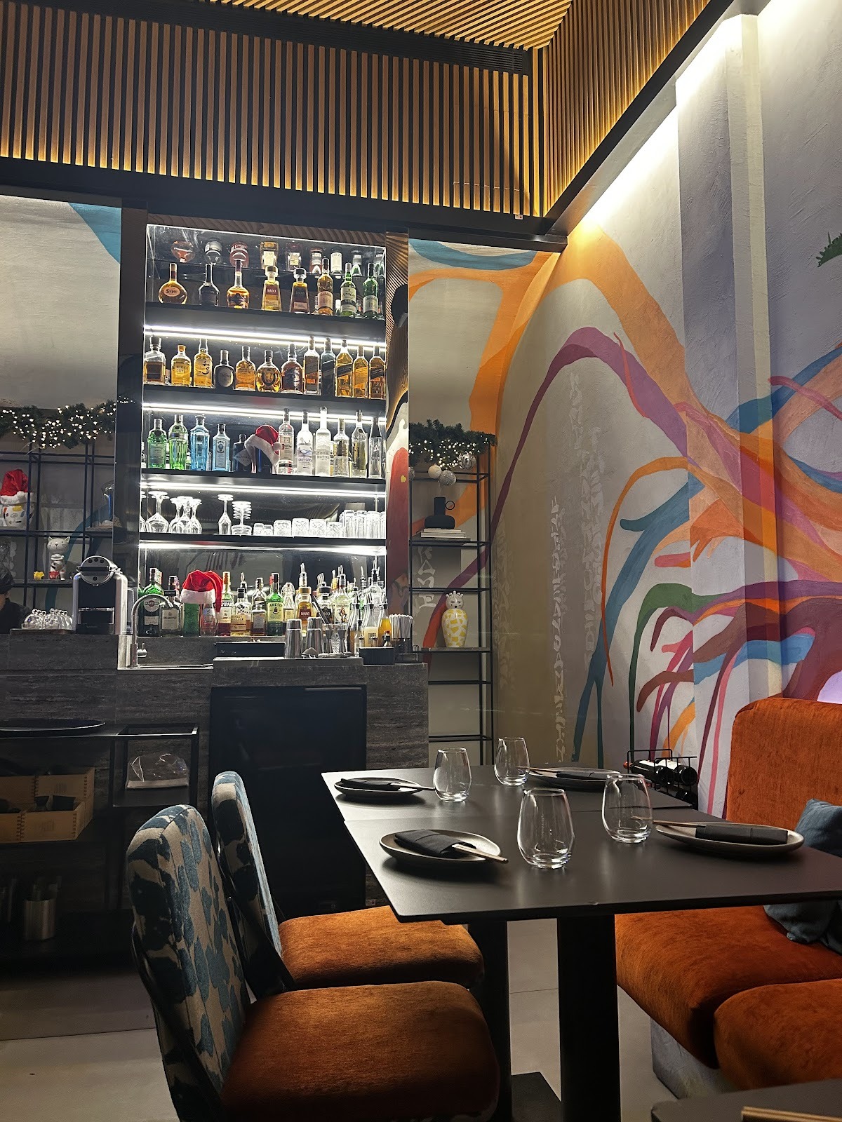 The bar shelf and the painted mural wall with orange velvet chairs at a set table