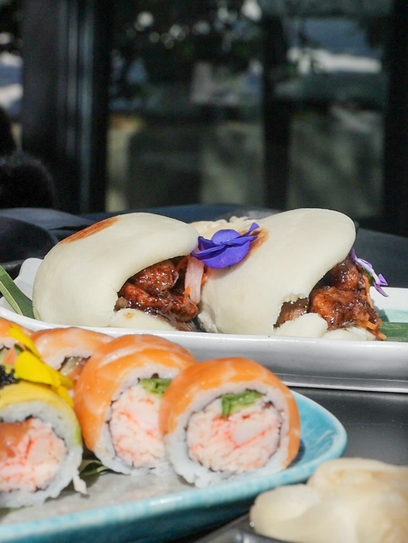 Bao buns with pulled beef beside a row of salmon rolls on a teal plate