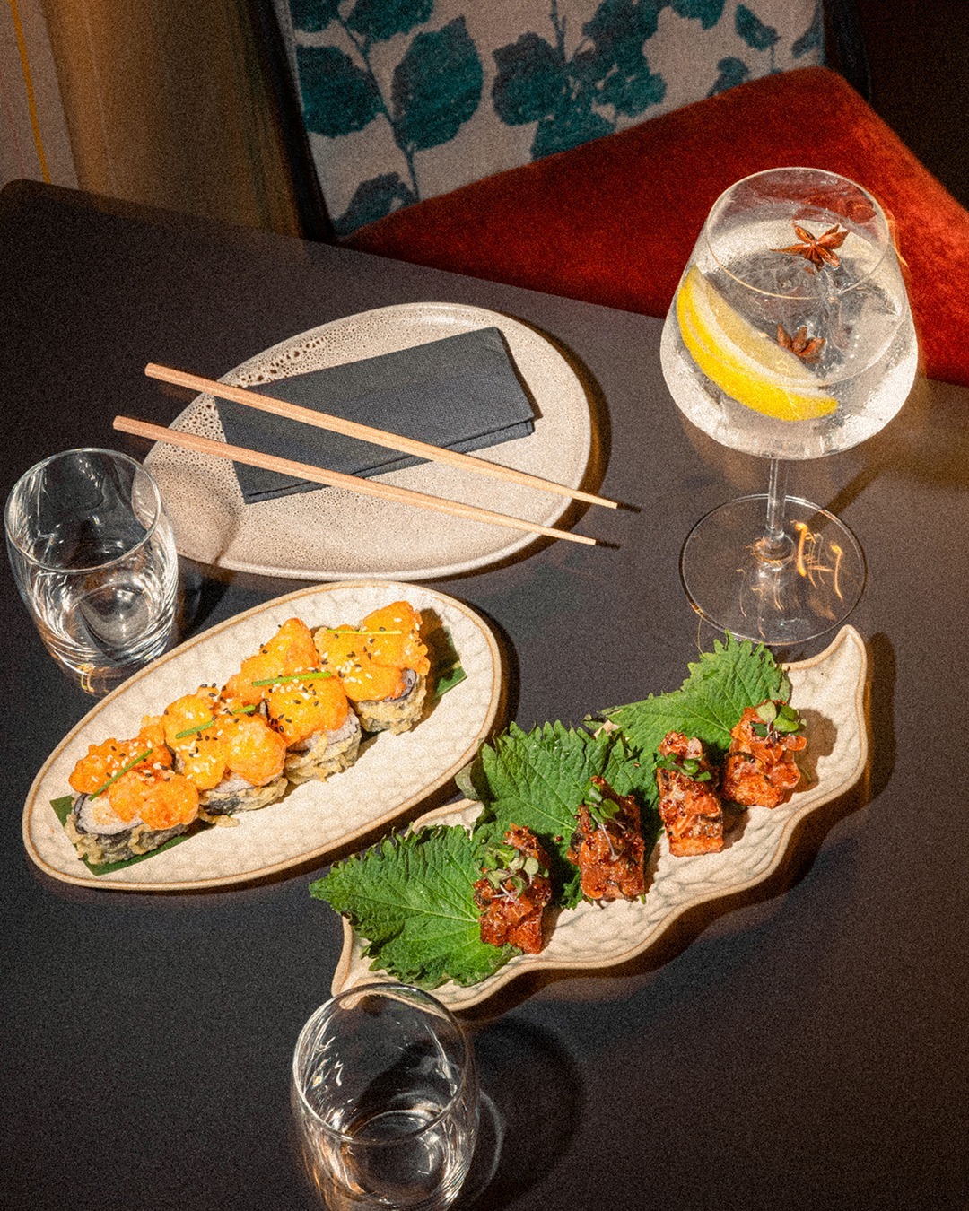 A boat plate and a leaf plate of rolls with a cold gin and tonic on the dining table