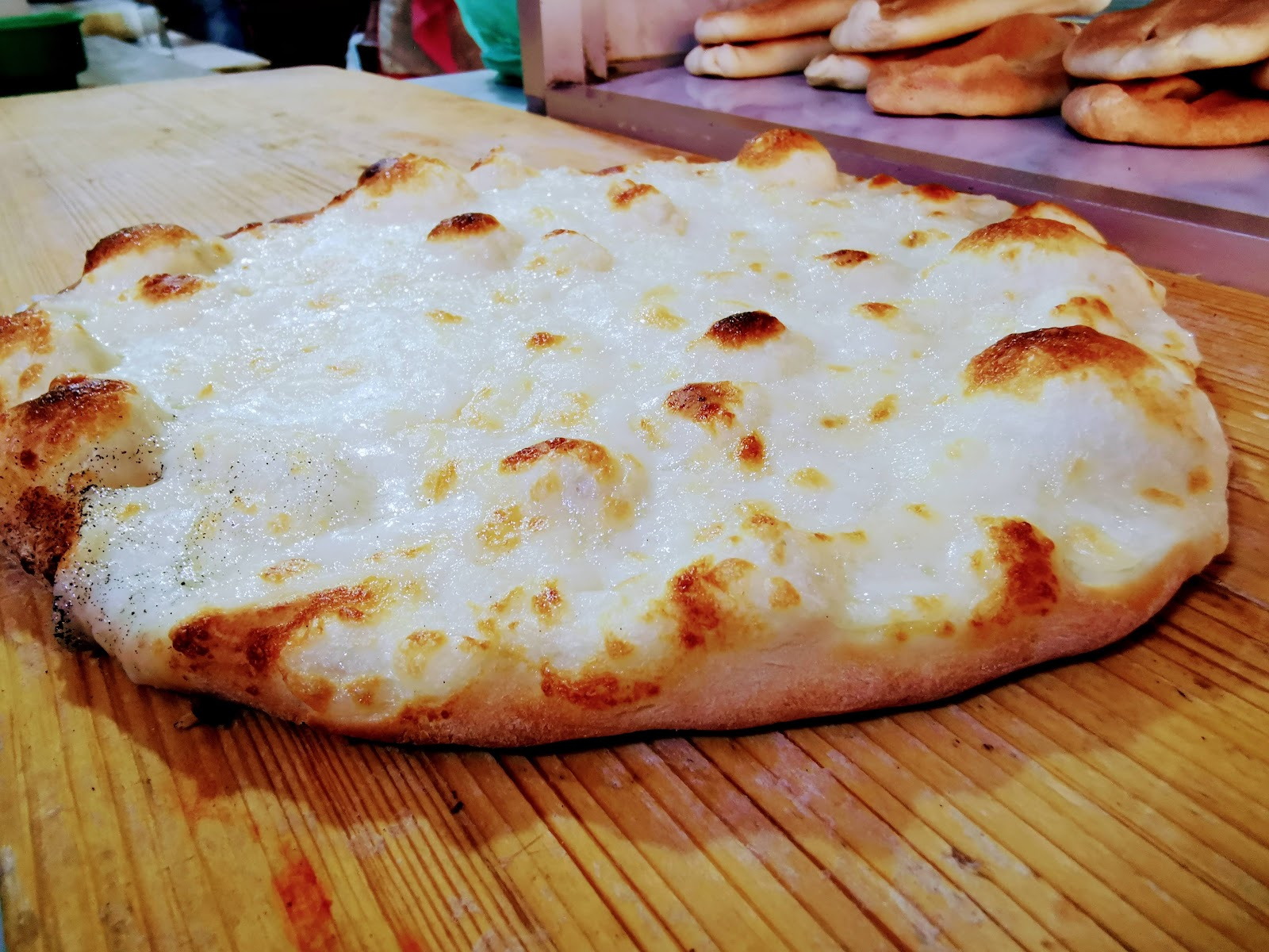 A wide cheese manoushe fresh off the peel on the wooden counter at Afran Maraach