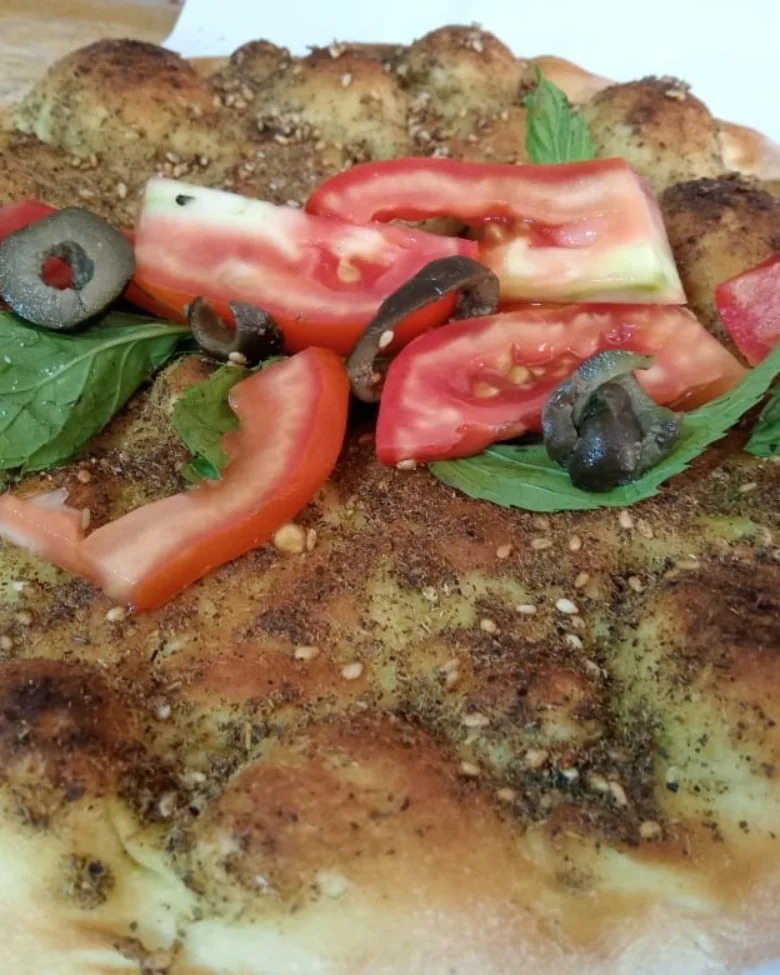 Za'atar manoushe topped with sliced tomato, olives and basil