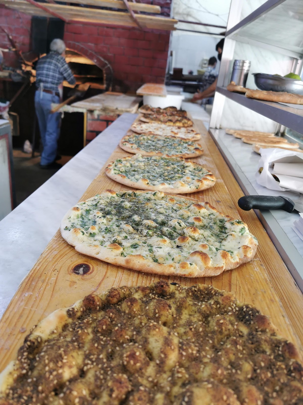 The long wooden counter at the furn with manakish lined up toward the oven