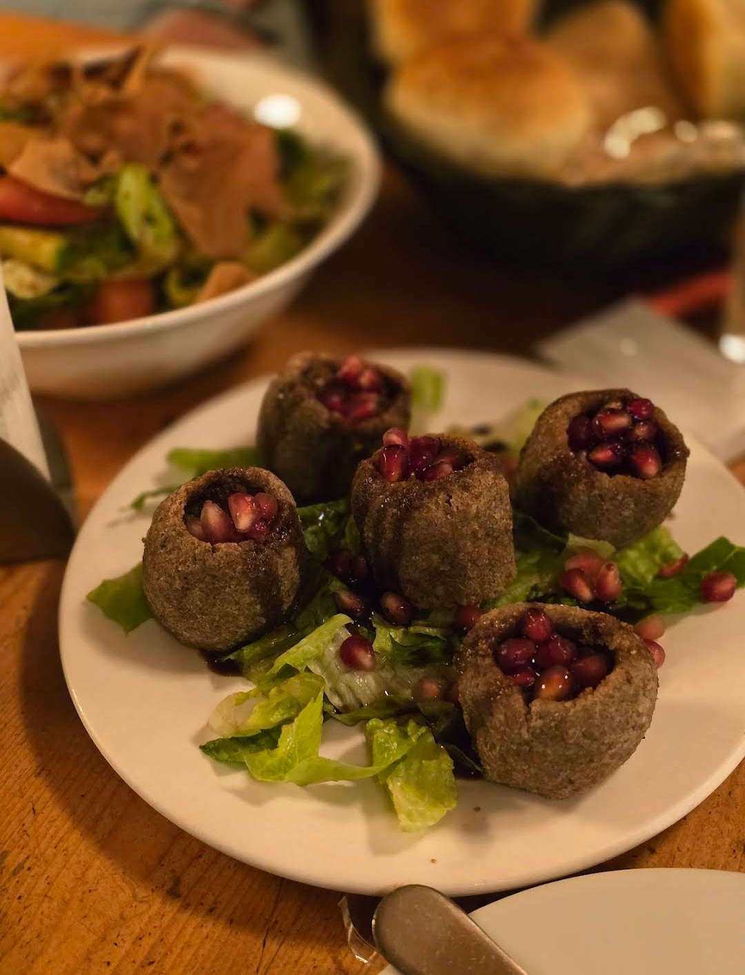 Kibbeh balls opened over lettuce with pomegranate seeds