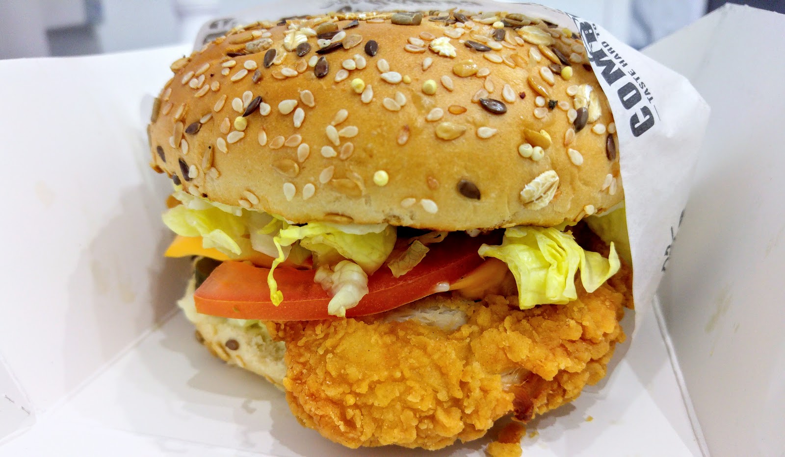 A seeded-bun burger with lettuce and tomato in branded wrap