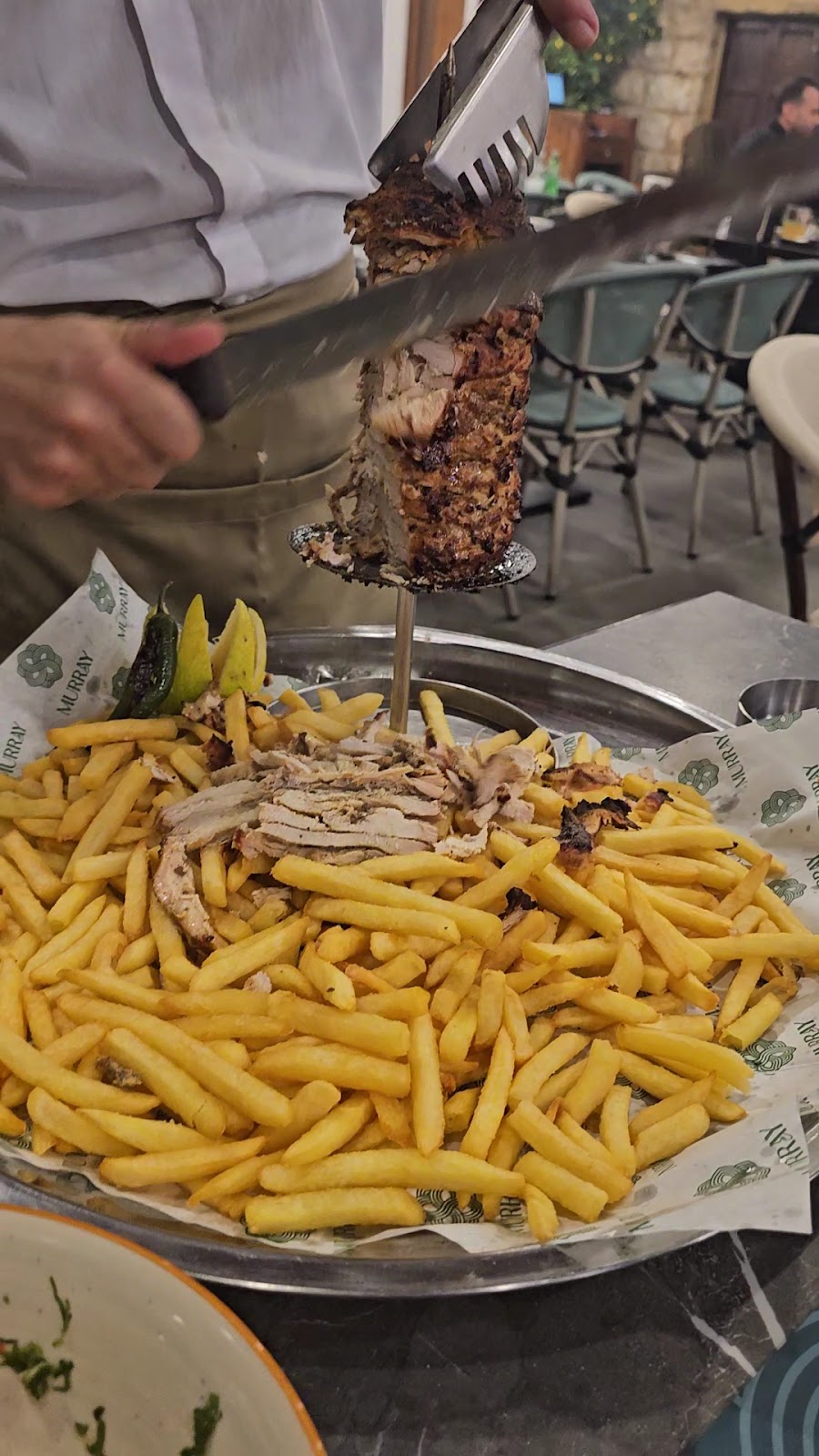 Carving the shawarma off the tabletop spit onto the fries