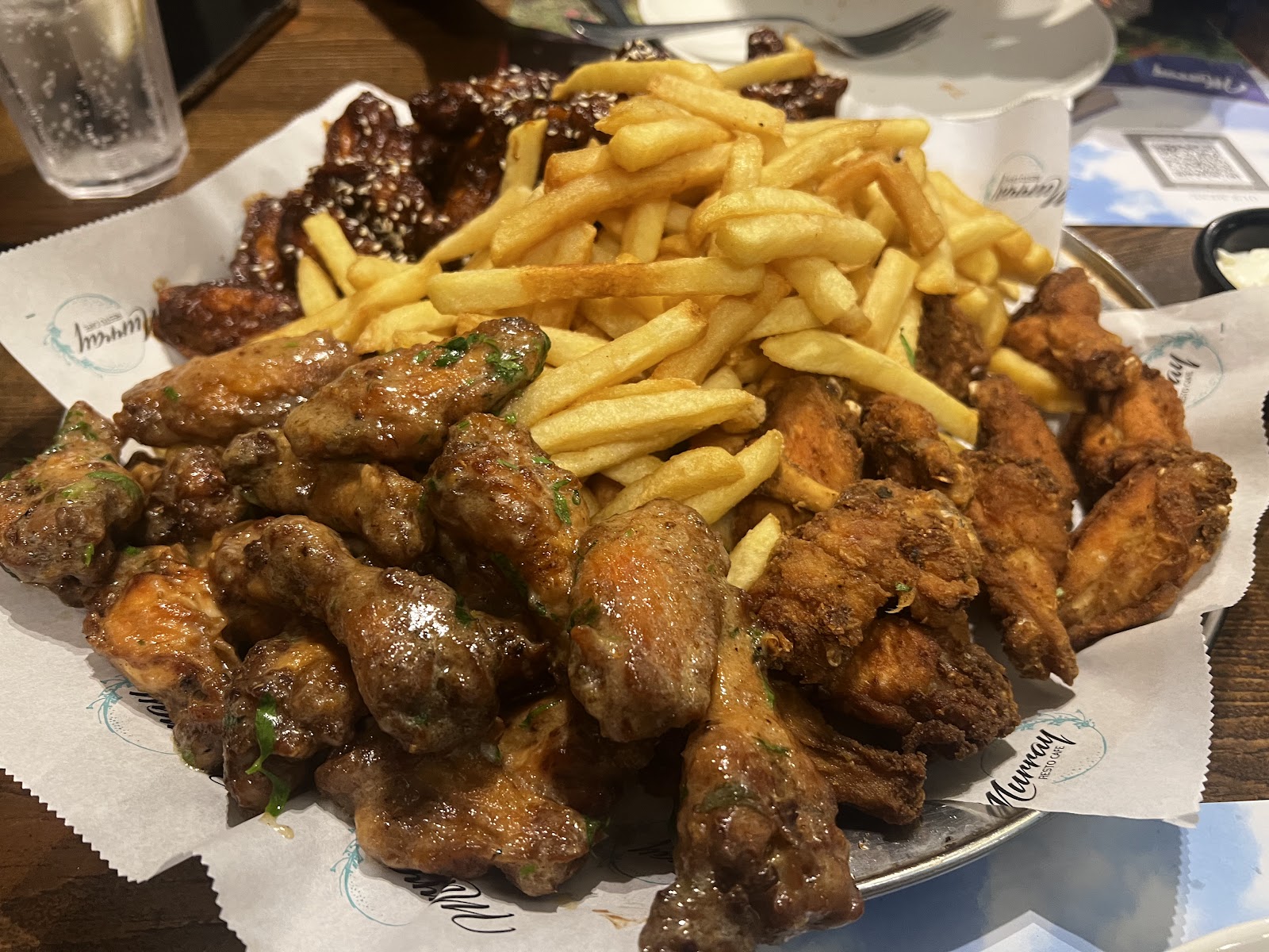 A pile of glazed wings with fries on branded paper