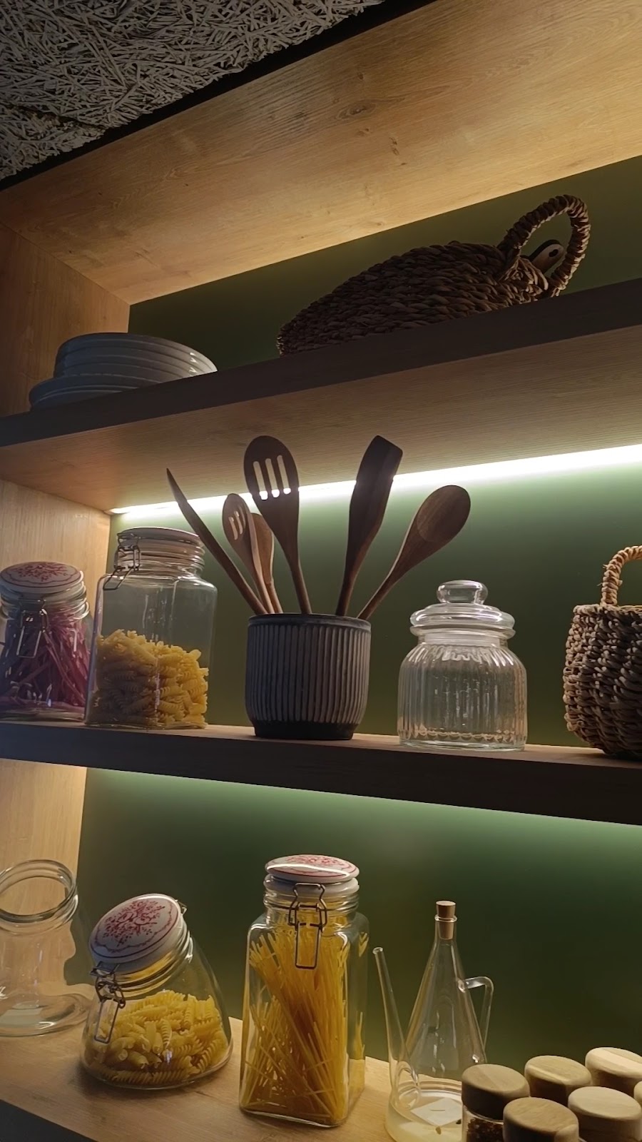 The lit shelf of jars, pasta and tools above the pass