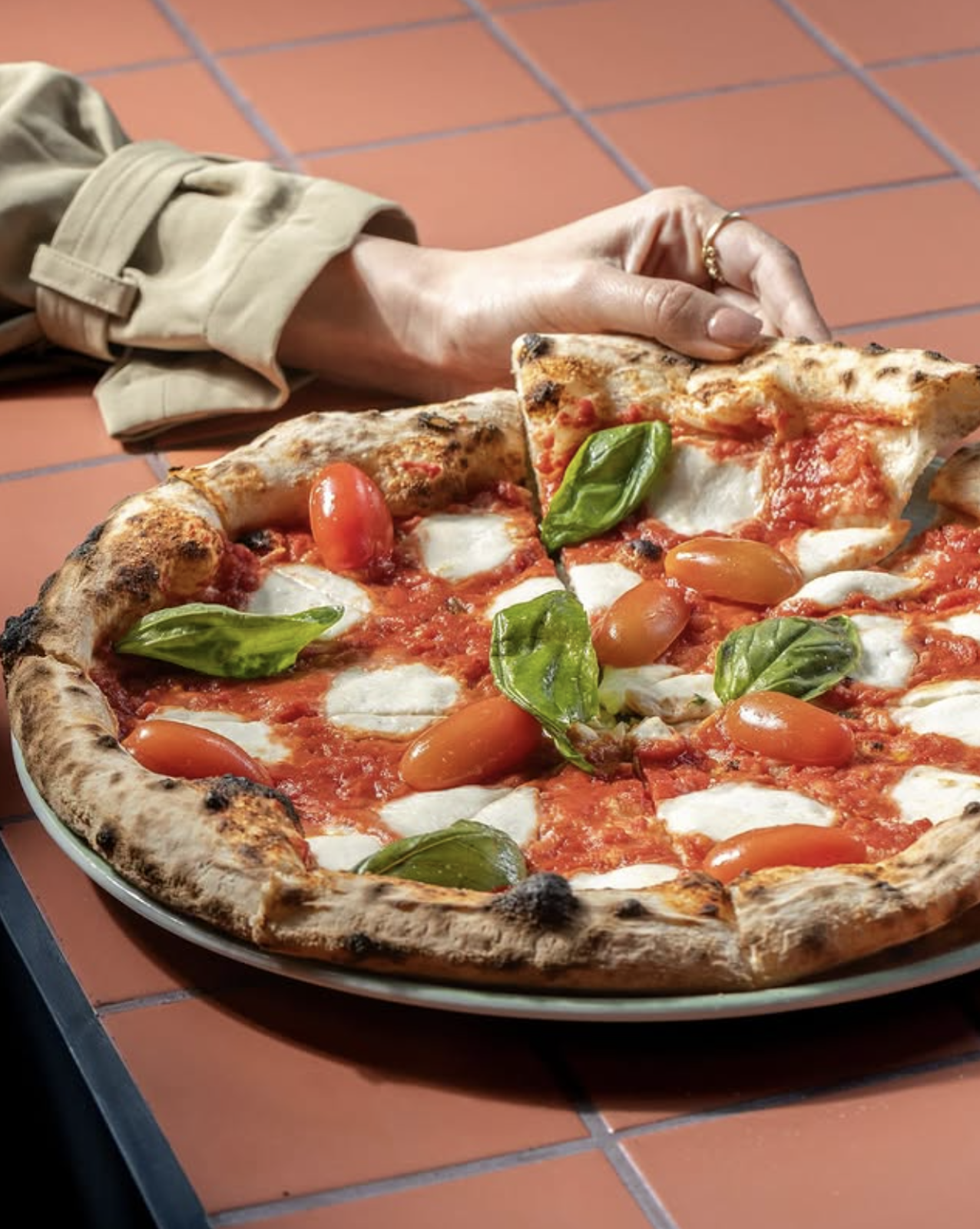 A margherita pizza held up over the terracotta floor