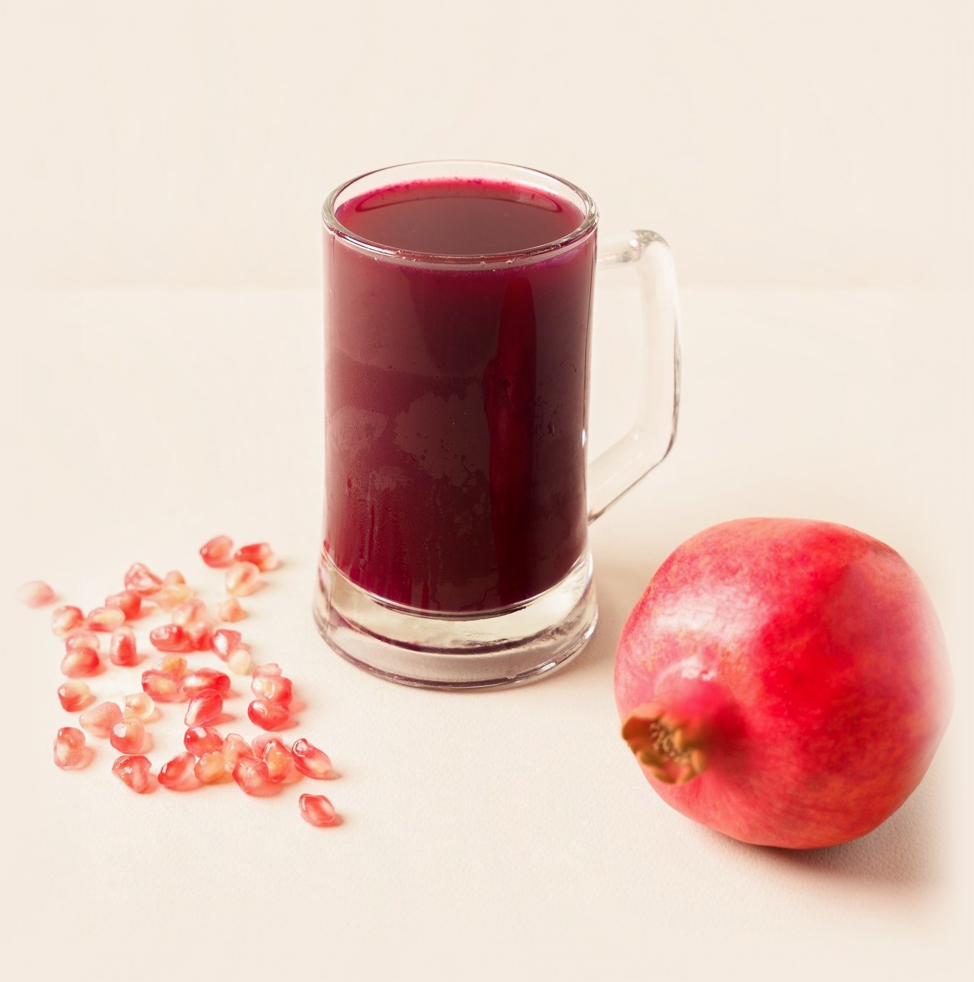 A tall glass mug of Ramadan Juice pomegranate juice beside a whole pomegranate and loose seeds