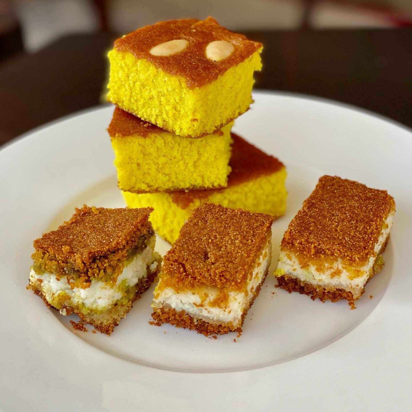 A stack of sfouf squares beside kishta fingers on a white plate