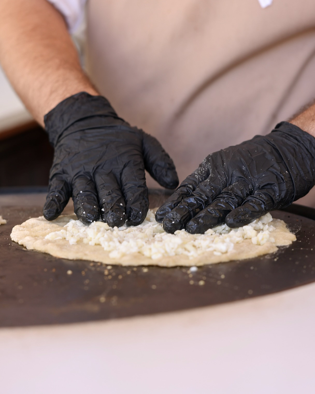 Hands spreading the topping over the dough on the black saj dome