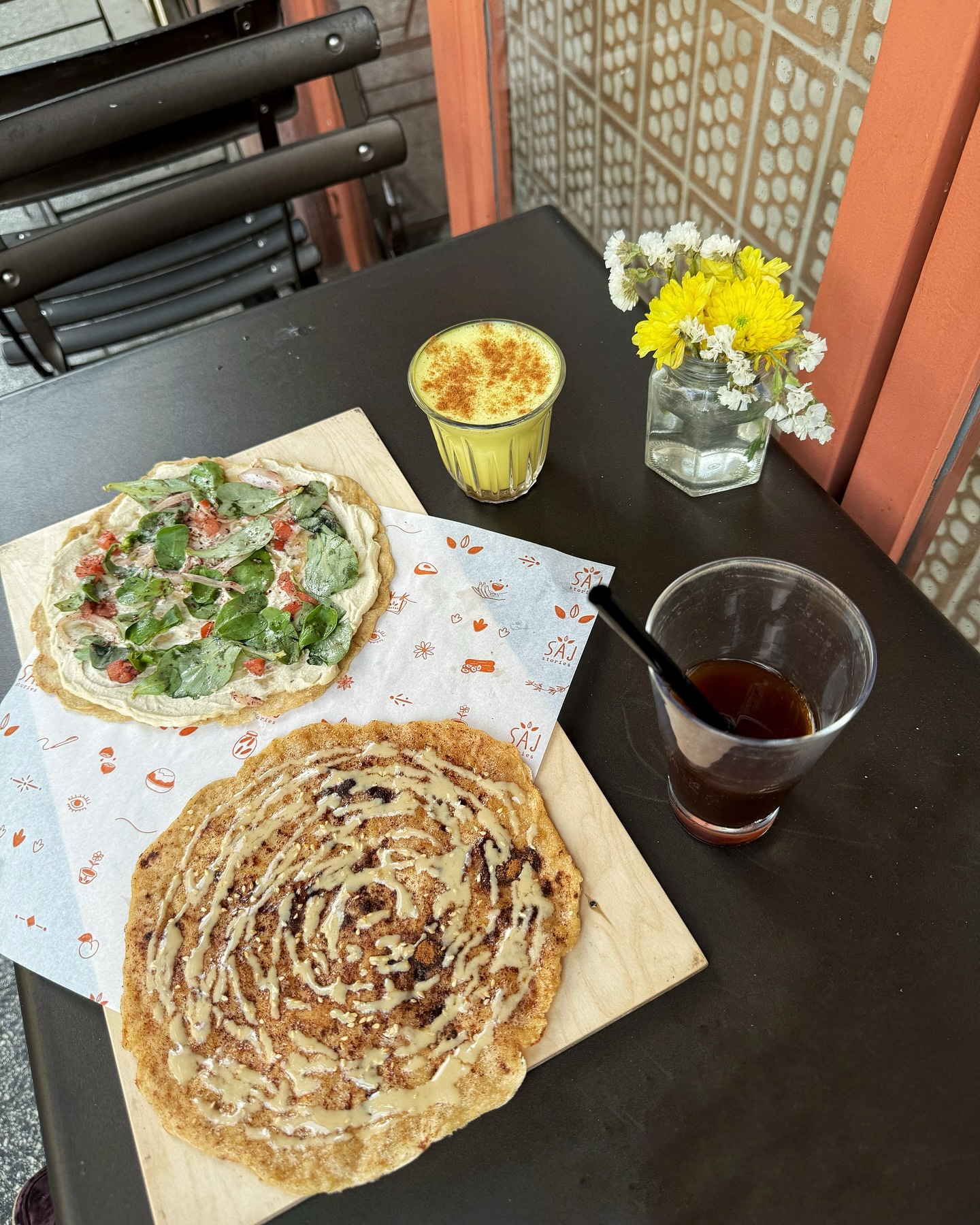 A table on the terrace with two saj on the shop's printed paper and two drinks