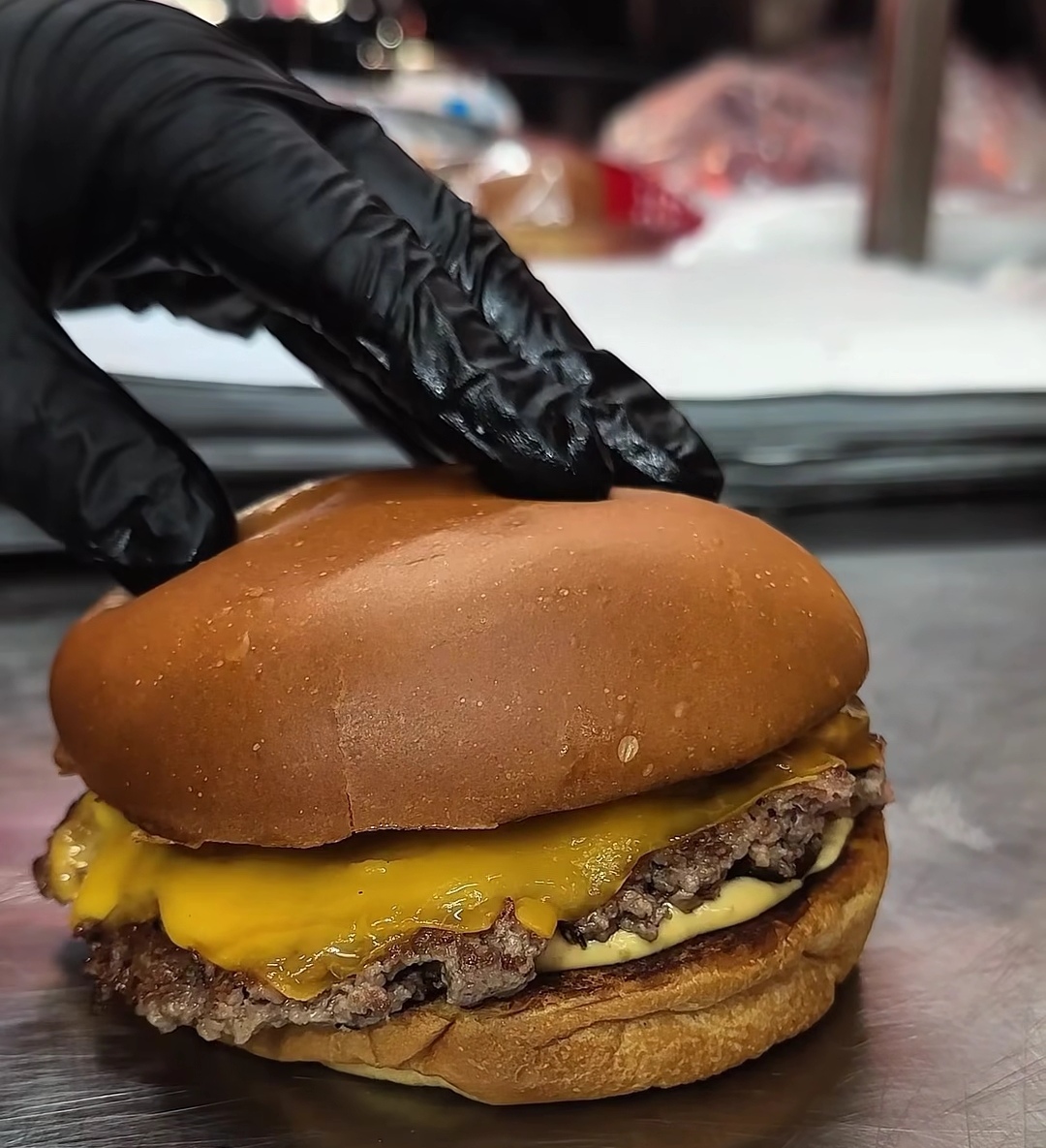 A gloved hand setting the bun on a fresh smash burger on the pass