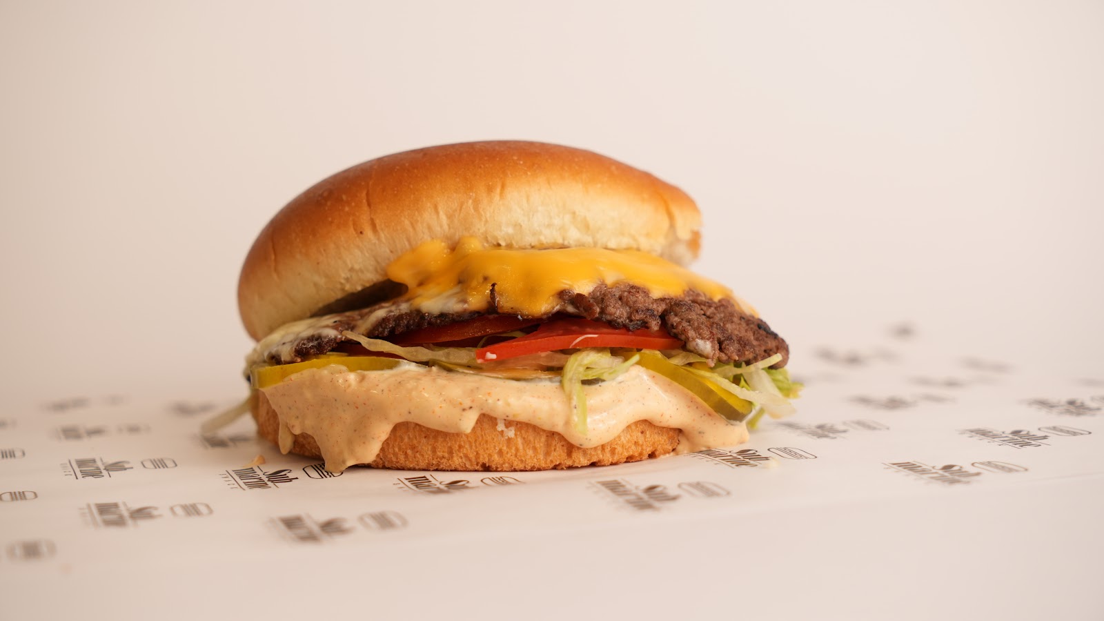 A cheeseburger with tomato and pickles on branded paper